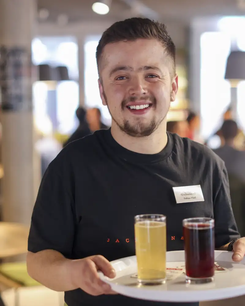 Ein Mitarbeiter eines Cafés trägt ein Tablett mit Getränken