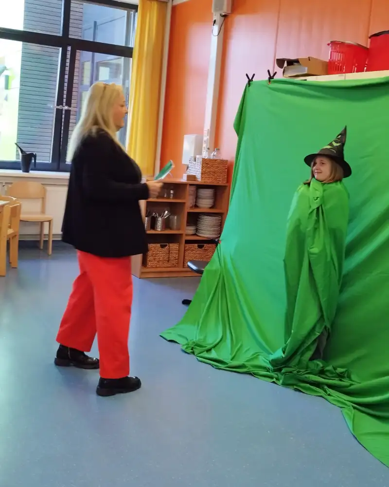 Ein Mädchen mit Hexenhut in einem grünen Tuch wird von einer Frau mit dem Handy gefilmt