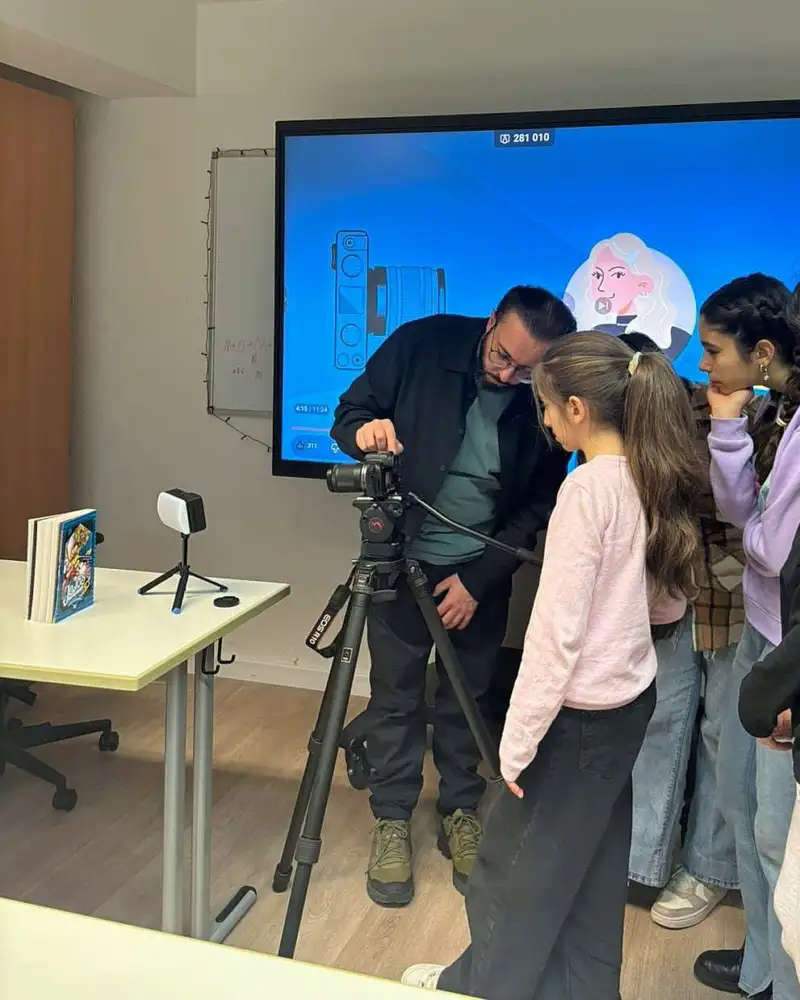 Ein Mann erklärt einer Gruppe von Kindern eine Fotokamera auf einem Stativ.