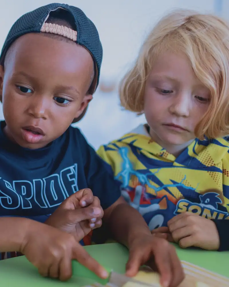 Zwei dunkelhäutige und ein blonder Junge im Kindergartenalter. Einer von ihnen schneidet einen Apfel in Stücke.