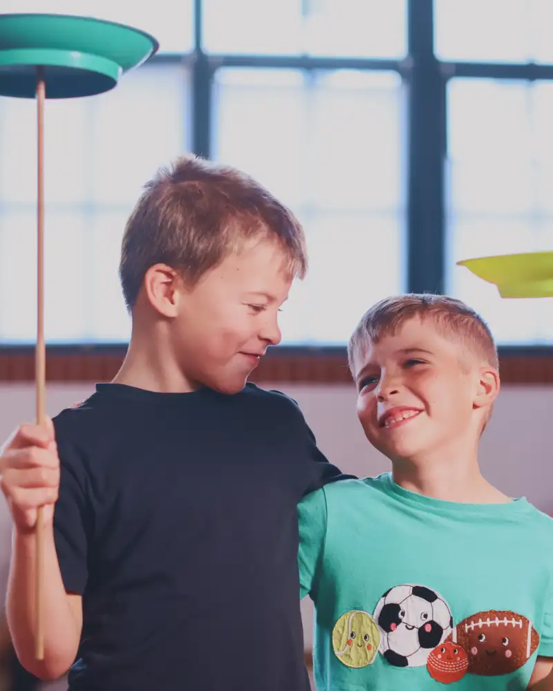 Zwei Jungen mit Jonglierstäben, auf denen eine bunte Scheibe rotiert.