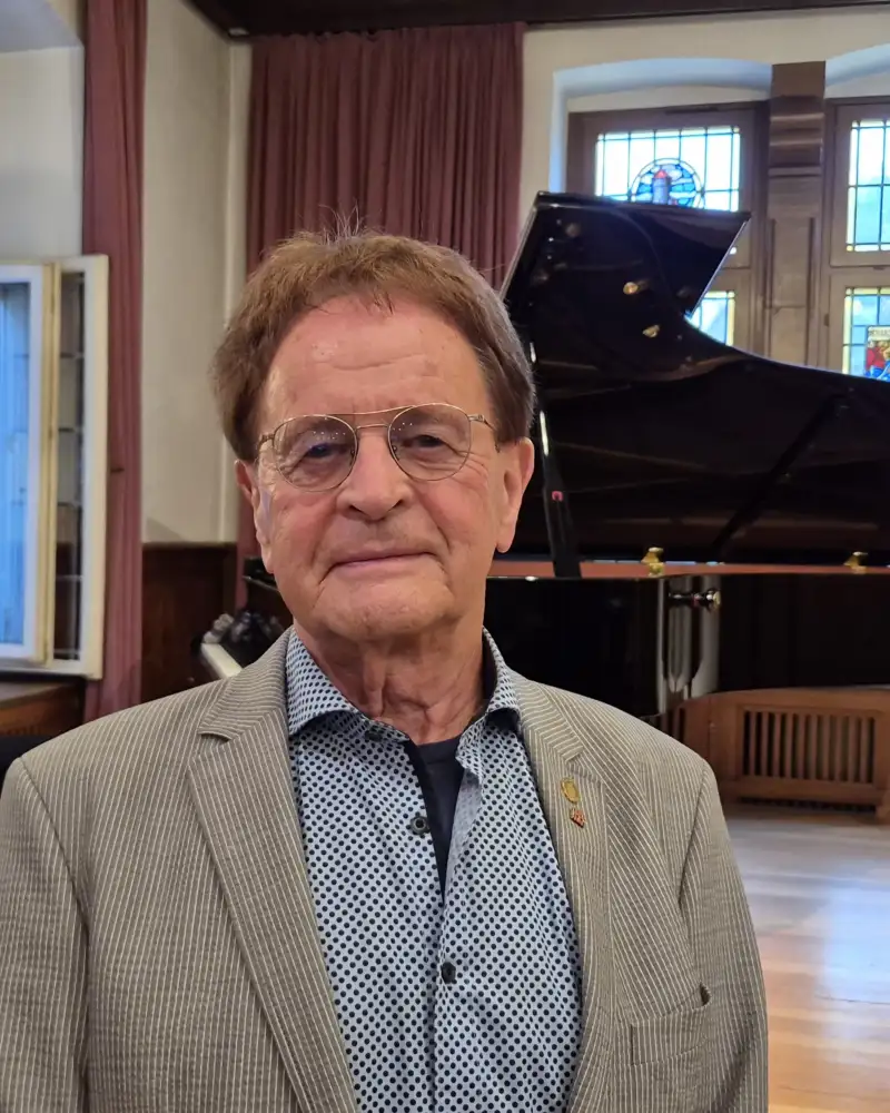 Ulrich Lange, der Gründer des Festivals für gute Taten, steht in einem Saal mit Flügel und Butzenscheiben.