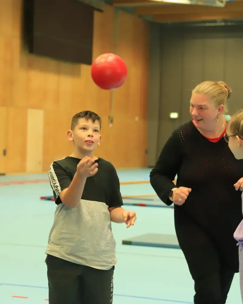 Zwei Erwachsene und zwei Kinder beim Ballspiel in einer Sporthalle