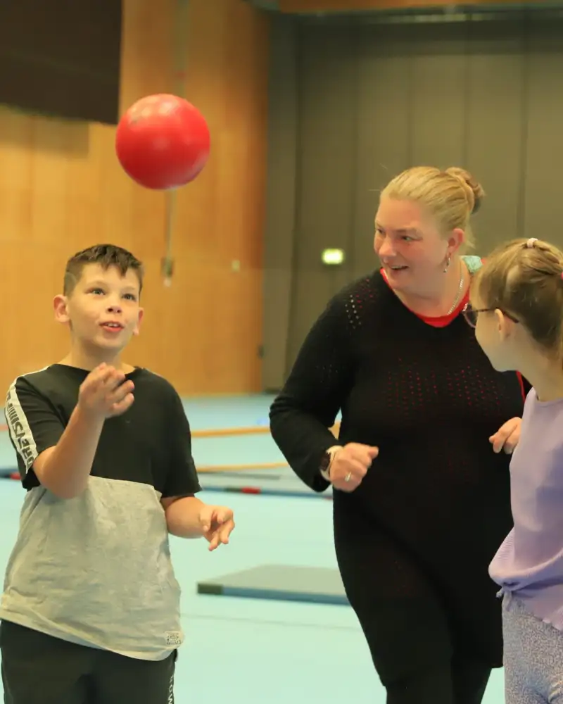 Zwei Erwachsene und zwei Kinder beim Ballspiel in einer Sporthalle