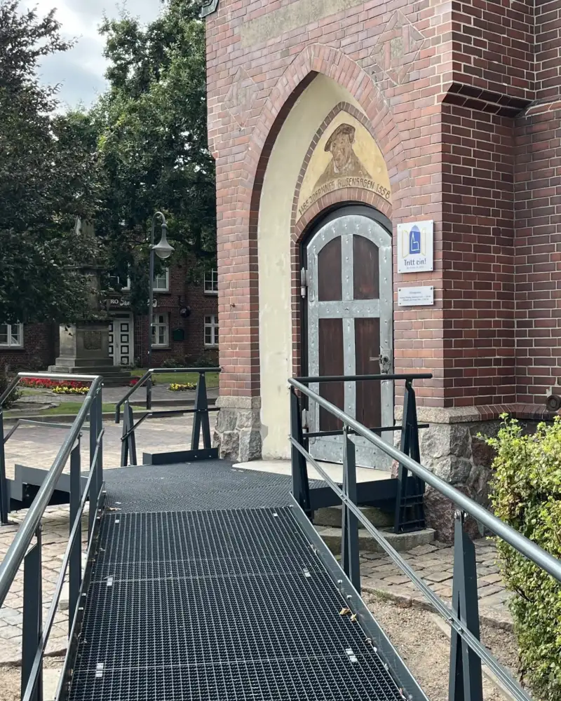 Eine lange Rampe führt zum Eingang einer Backsteinkirche.