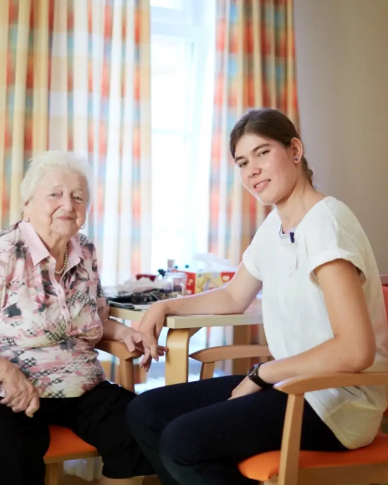 Eine Seniorin und eine Pflegerin sitzen an einem Tisch