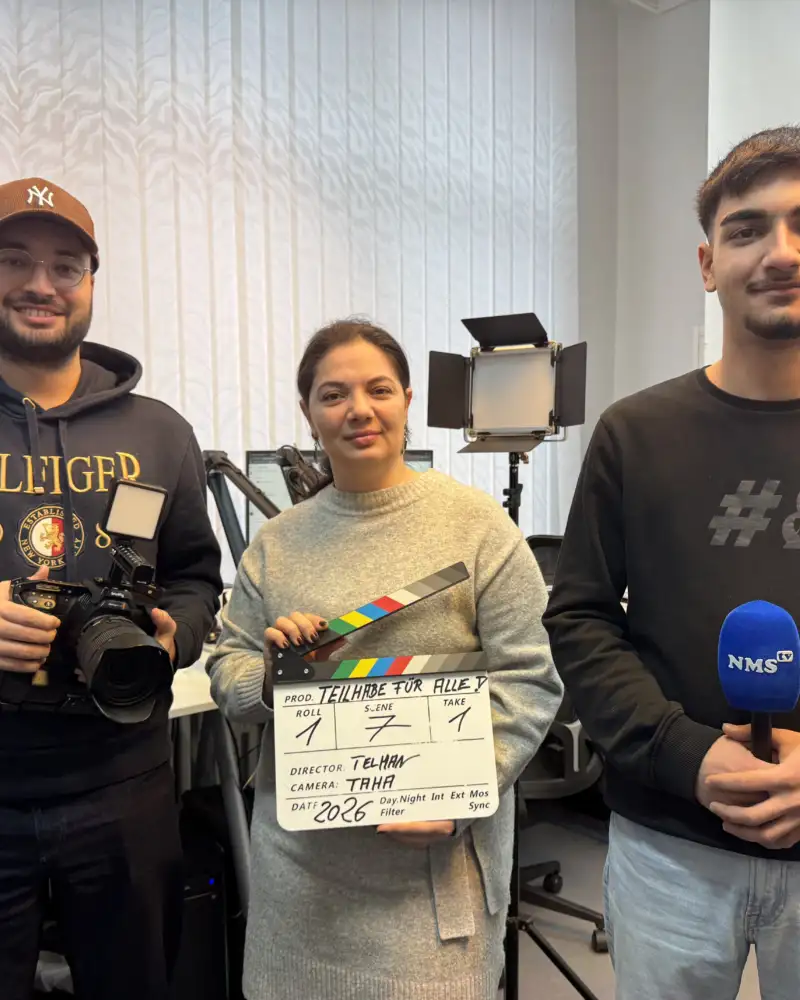 Zwei Männer und eine Frau. Sie tragen eine Filmkamera, eine Regieklappe und ein Mikrofon.