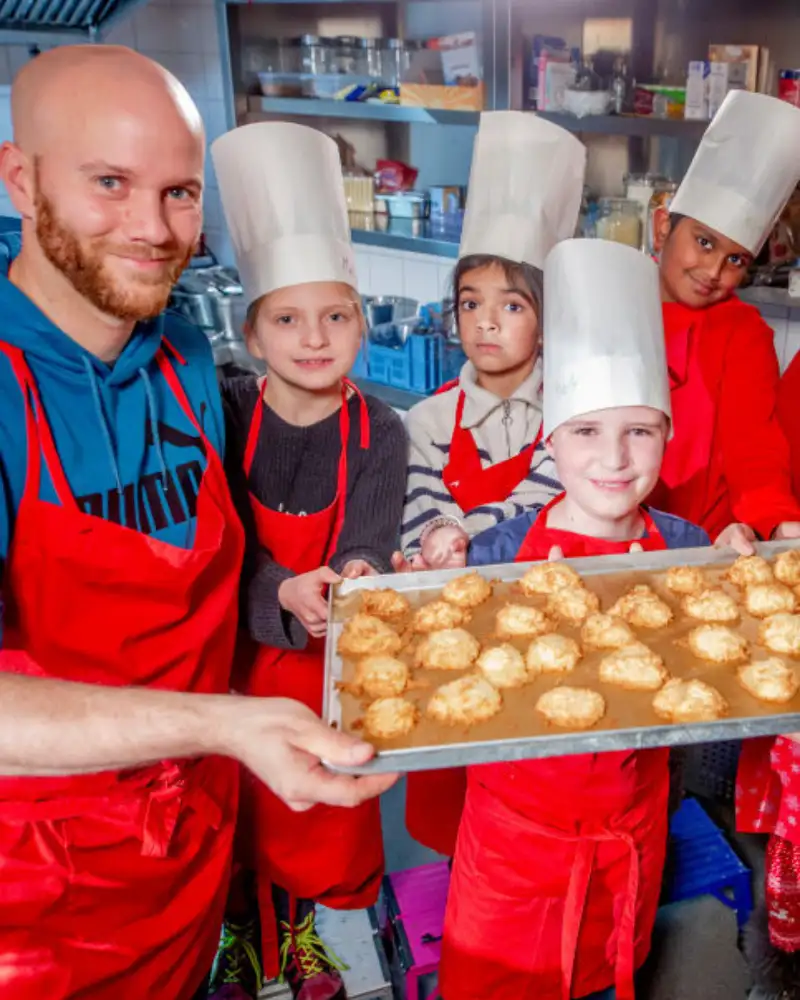 Mehrere Kinder und Erwachsene zeigen Backbleche mit Backwaren