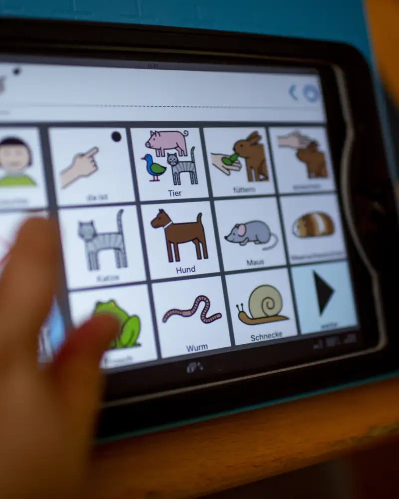 Eine Kinderhand tippt auf den Bildschirm eines Tablets. Darauf sind Piktogramme verschiedener Tiere abgebildet.