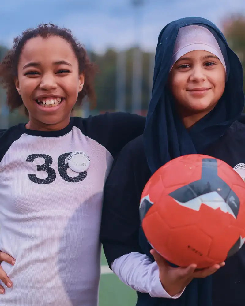 Zwei Mädchen mit Migrationshintergrund mit einem Ball auf einem Spielfeld
