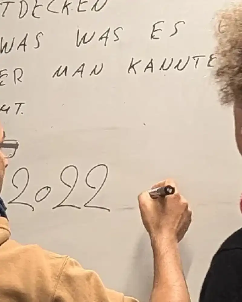 Zwei Männer, die von hinten zu sehen sind, stehen vor einem beschriebenen Flipchart. Einer von beiden schreibt etwa neben die Zahl 2022.