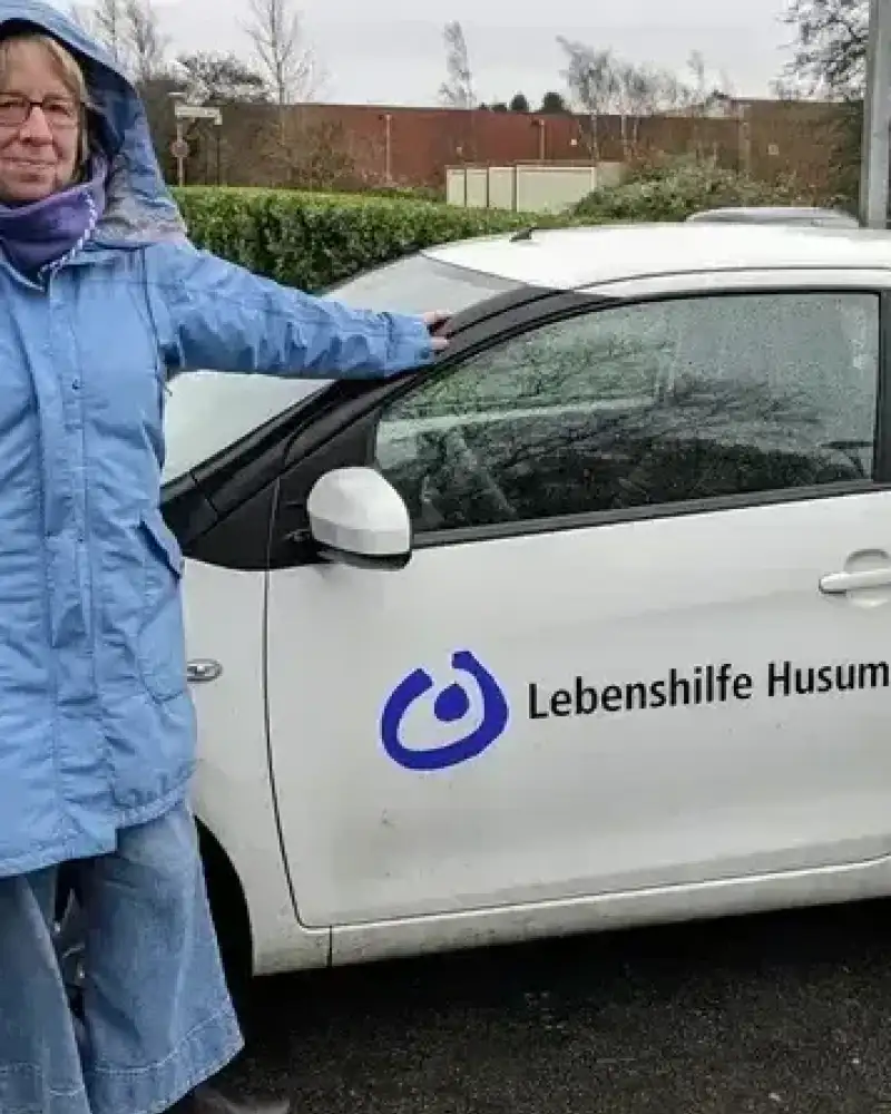 Zwei Männer in Parkas lehnen an einem weißen Wagen mit der Aufschrift Lebenshilfe Husum.