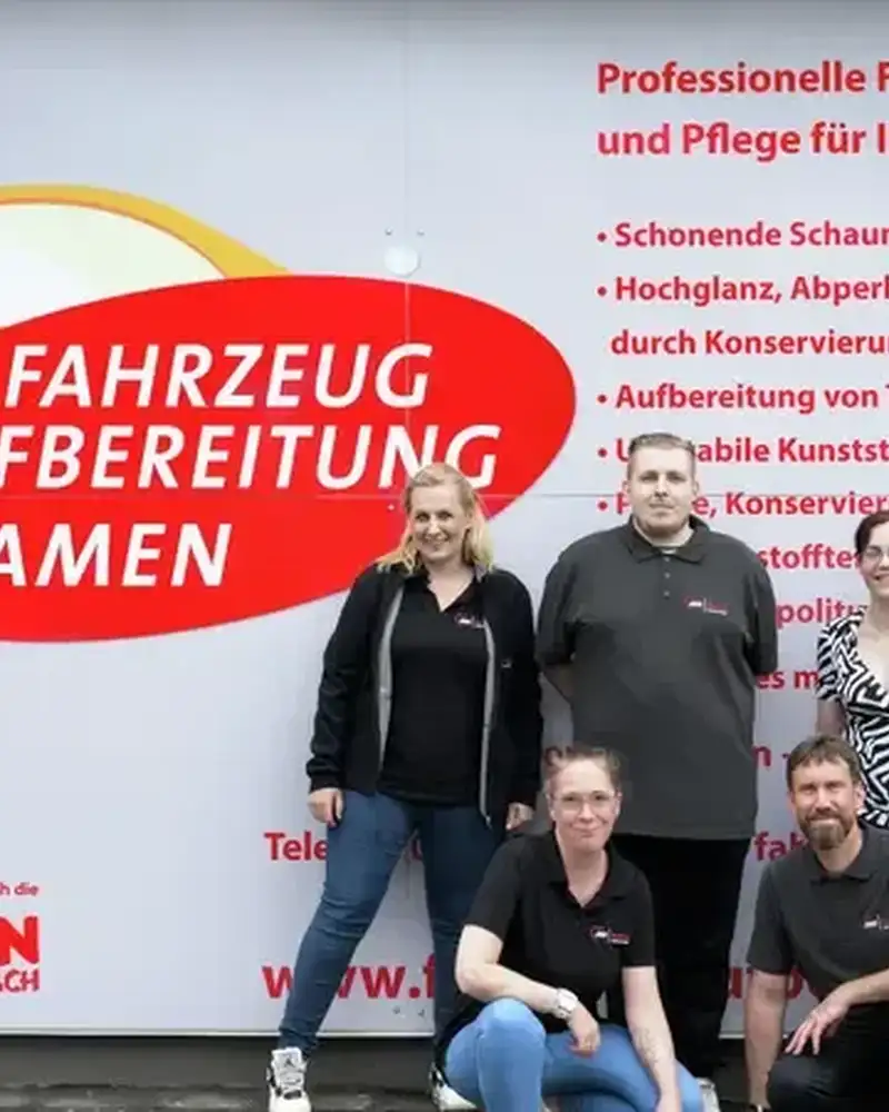 Sechs Personen stehen vor einem großen Plakat. Darauf steht unter anderem: "Fahrzeug Aufbereitung Kamen".