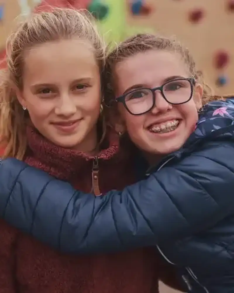 Ein Mädchen mit Brille und Zahnspange umarmt ein anderes Mädchen.