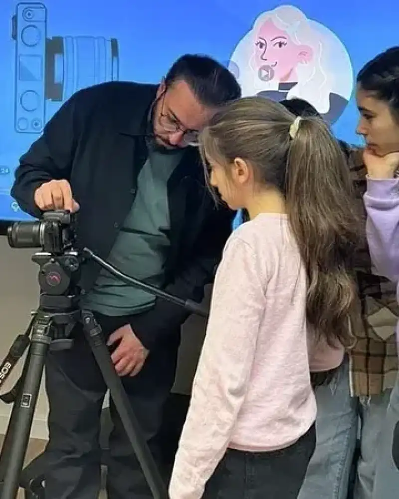 Ein Mann erklärt einer Gruppe von Kindern eine Fotokamera auf einem Stativ.