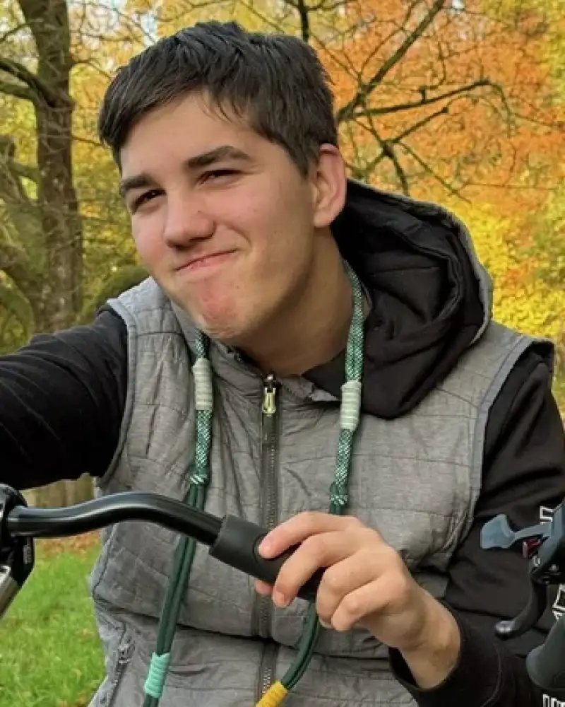 Ein junger Mann ist mit dem Rad unterwegs. Er hält den rechten Daumen hoch.