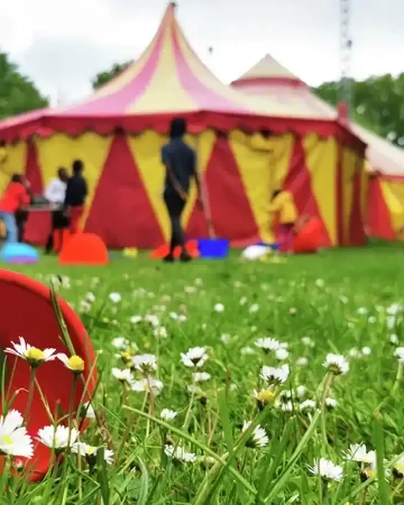 Ein rotes Diabolo liegt auf einer Wiese vor einem Zirkuszelt