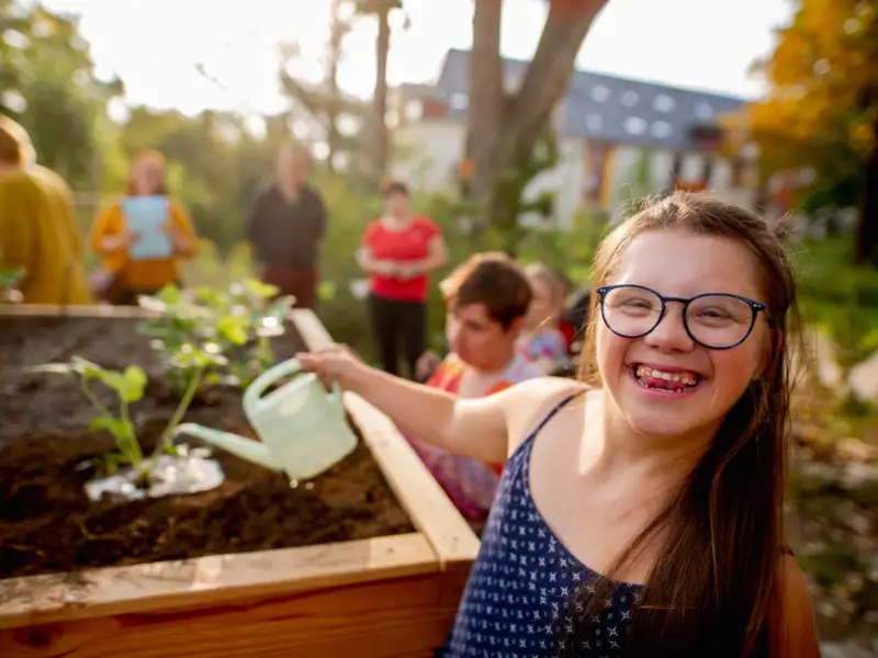 Ein Mädchen mit Downsyndrom gießt ein Hochbeet.