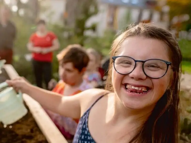 Ein Mädchen mit Downsyndrom gießt ein Hochbeet.