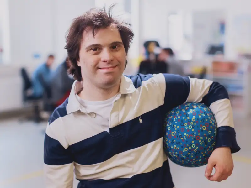 Ein junger Mann im geringelten Polohemd hat einen Ball unterm Arm.