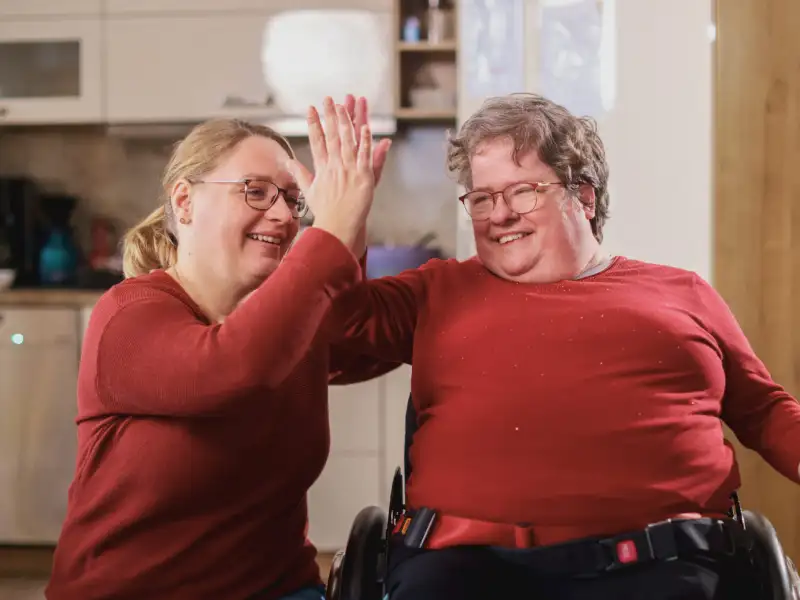 Eine Frau gibt einer anderen Frau im Rollstuhl High Five