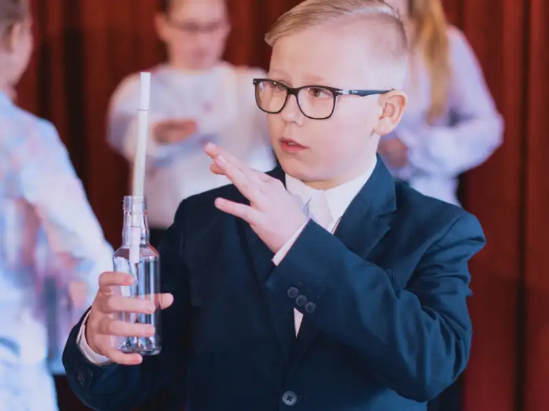 Ein Junge macht einen Zaubertrick mit einer Glasflasche, in der ein Zettel steckt