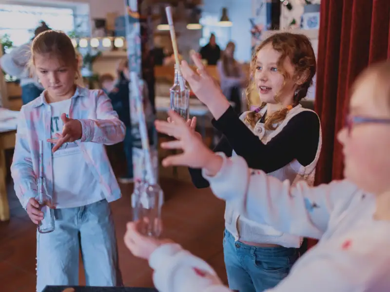 Drei Kinder machen einen Zaubertrick mit Glasflaschen, in denen Zettel stecken