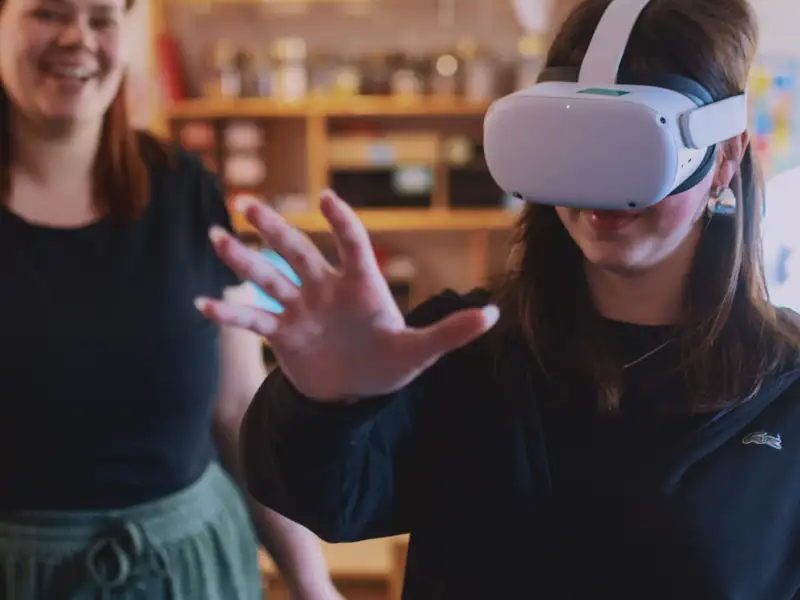Ein Mädchen mit VR Brille, im Hintergrund steht eine lächelnde Frau