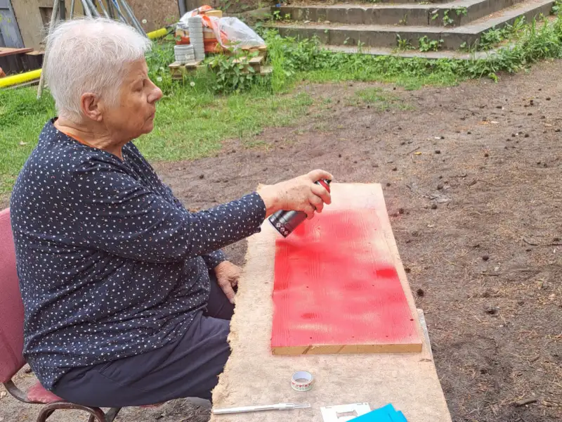Eine Frau sitzt im Freien und sprüht rote Farbe auf ein Schild