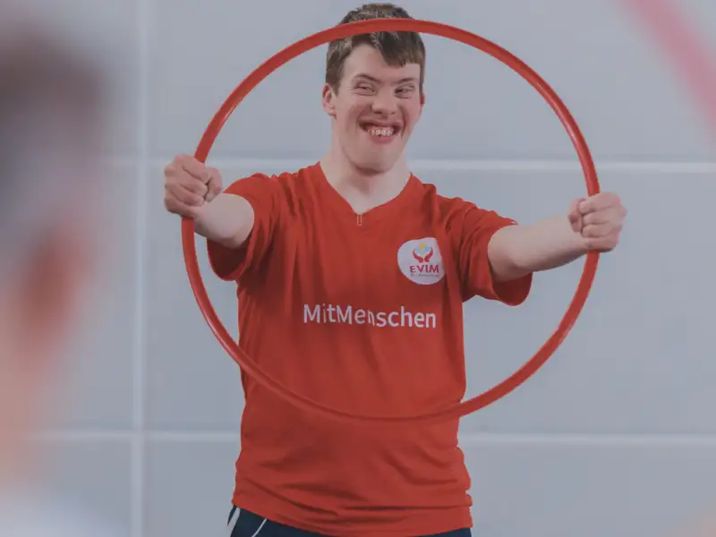 Ein junger Mann mit Downsyndrom hält einen Hula Hoop Reifen in die Höhe