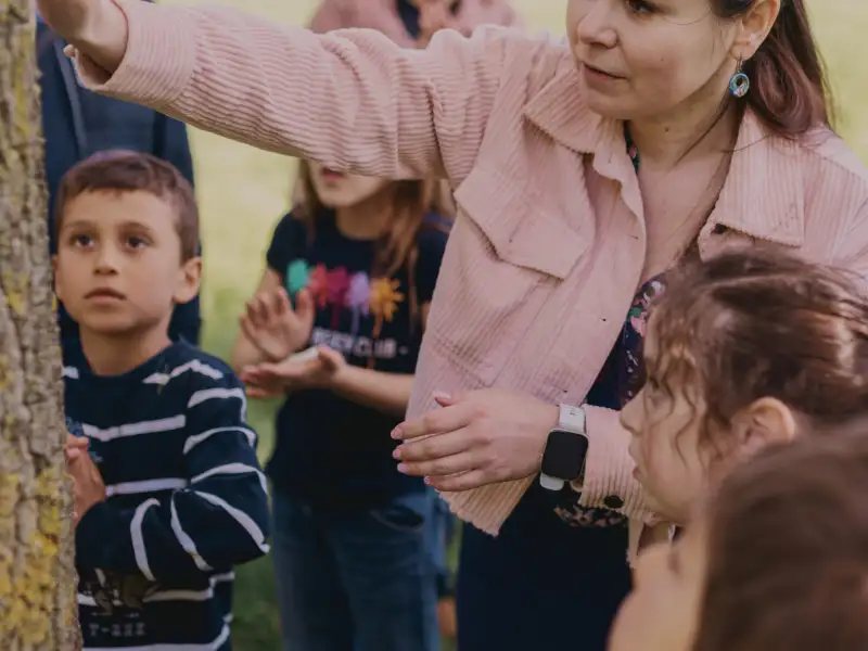 Eine junge Frau und mehrere Kindre stehen neben einem Baumstamm