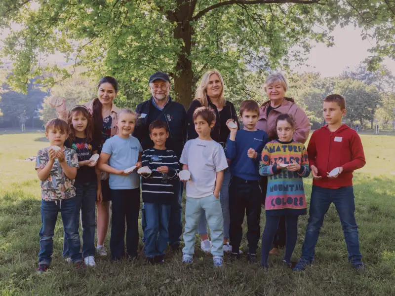 Eine Gruppe von Kindern und einigen Erwachsenen auf einer Wiese unter einem Baum
