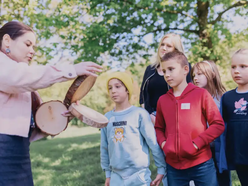 Eine junge Frau zeigt einer Gruppe Kindern verschiedene Baumscheiben