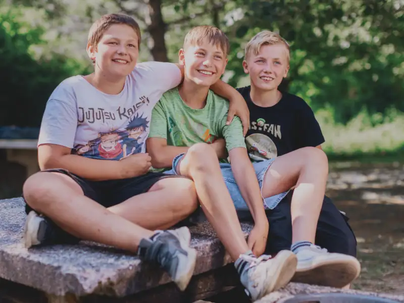Drei Jugendliche sitzen lächelnd nebeneinander
