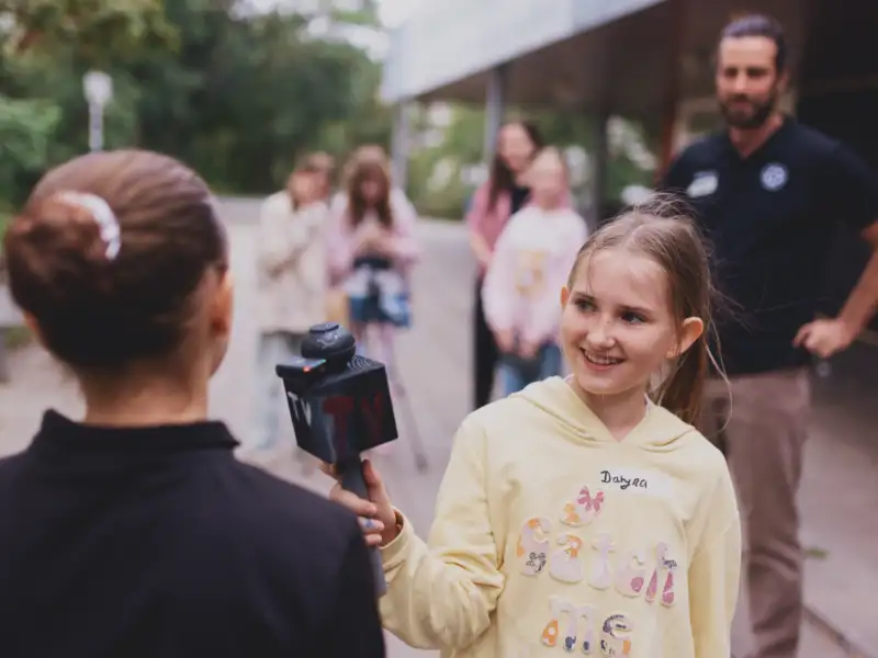 Ein Mädchen mit Mikrophon in der Hand interviewt ein anderes Mädchen