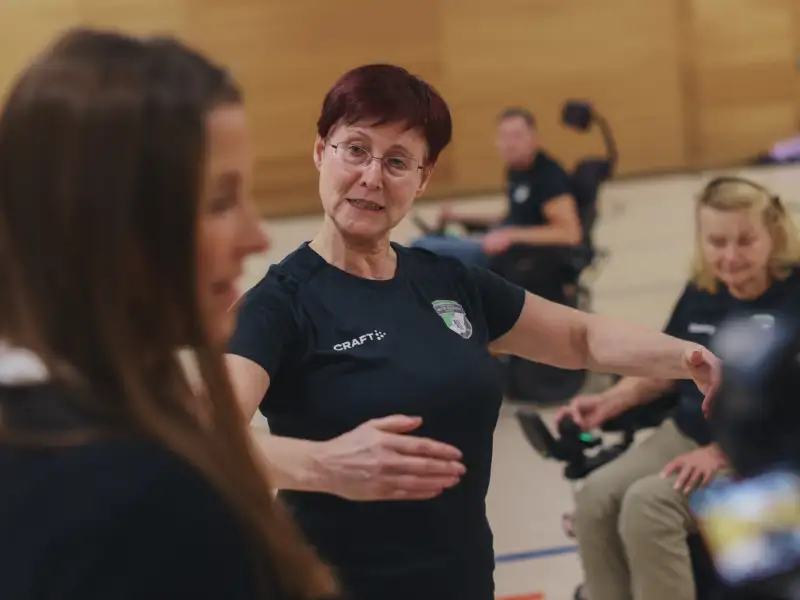 Eine Frau mit Brille zeigt zwei Frauen eine Tanzposition.