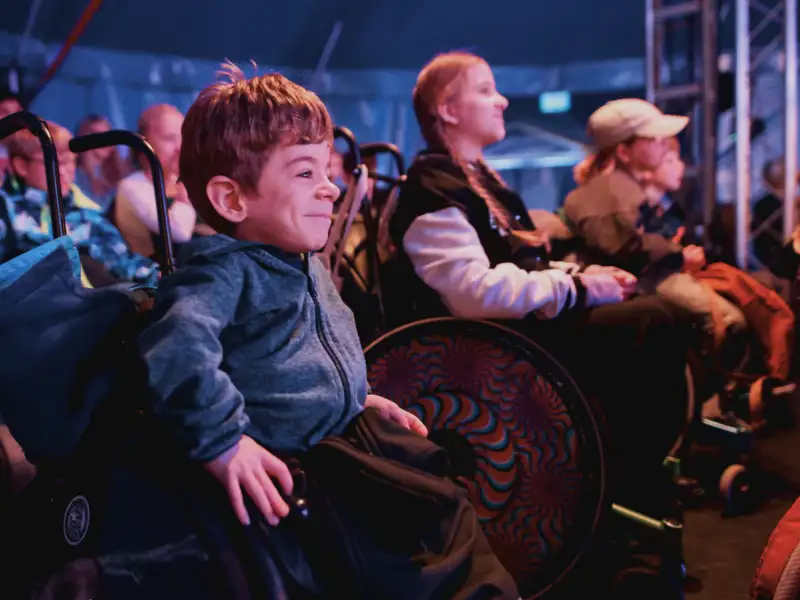 Mehrere Kinder in Rollstühlen sitzen im Zuschauerbereich eines Zirkus.