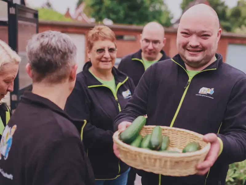 Ein Mann in einer Gruppe von Menschen zeigt einen Korb voller Zucchini.