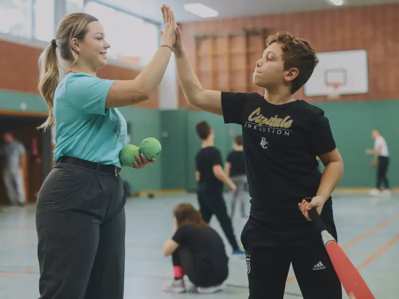 Eine junge Frau und ein Junge mit Baseballschläger klatschen sich ab.
