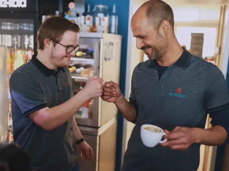 Ein junger Mann mit Down-Syndrom und ein älterer Mann lachen sich an.
