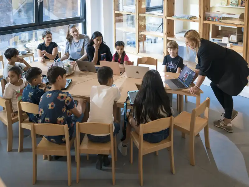 Kinder sitzen rund um einen großen Tisch und schauen auf einen Laptop