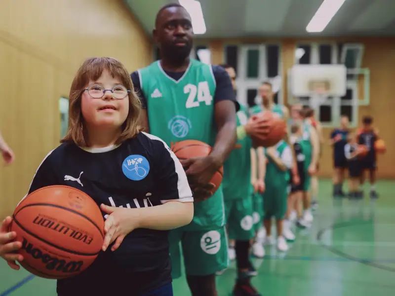 Mädchen mit Downsyndrom trägt auf einem Spielfeld einen Basketball