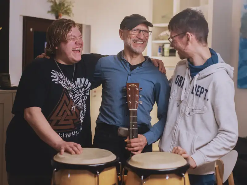 Drei junge Männer lachen sich an - zwei haben Bongos, einer eine Gitarre.