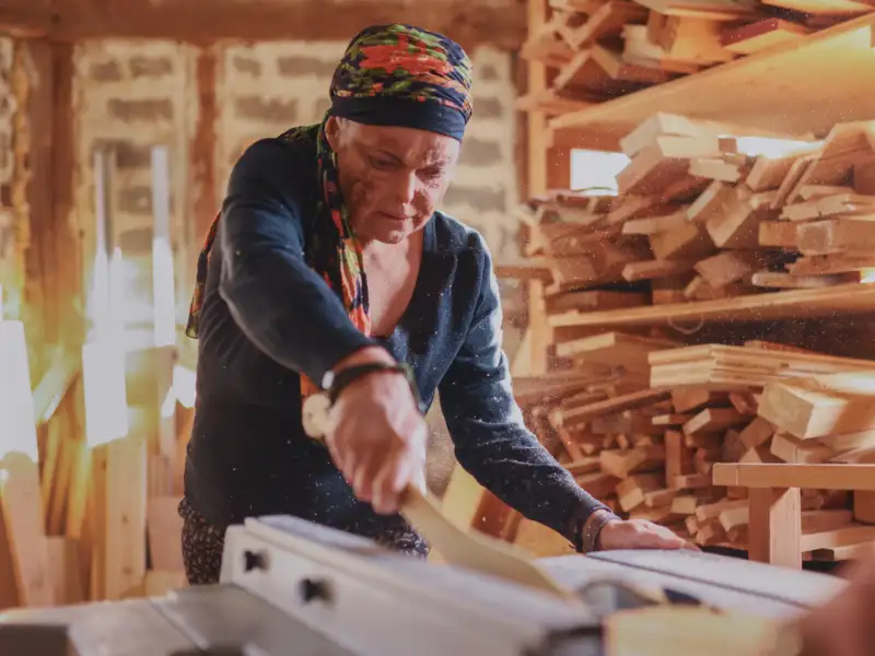 Eine Frau mit Kopftuch sägt ein Stück Holz zu.