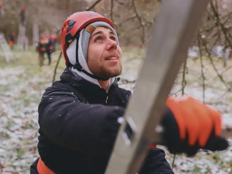 Ein junger Mann steht auf einer Leiter. Er trägt einen orangefarbenen Schhutzhelm.