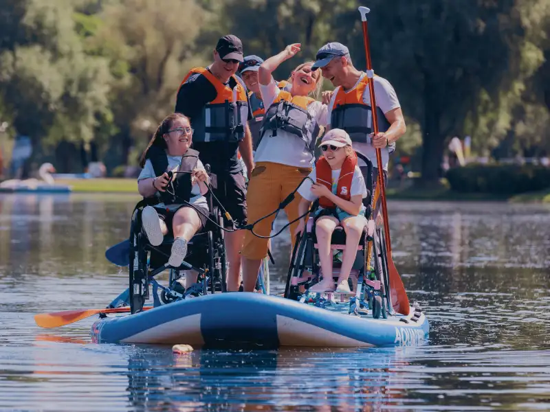 Mehrere Personen mit und ohne Rollstuhl gemeinsam auf einem großen Paddle-Board