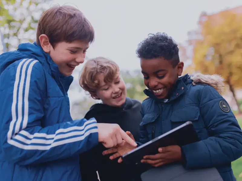 Drei Jungen schauen auf ein Tablet. Sie lachen.