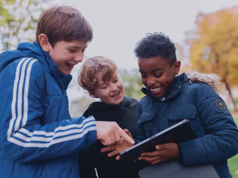 Drei Jungen schauen auf ein Tablet. Sie lachen.