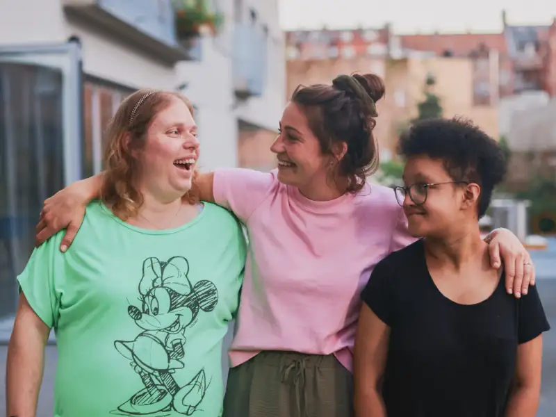 Drei junge Frauen stehen lachend Arm in Arm im Freien