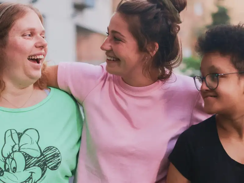 Zwei junge Frauen und ein Mädchen stehen lachend Arm in Arm im Freien